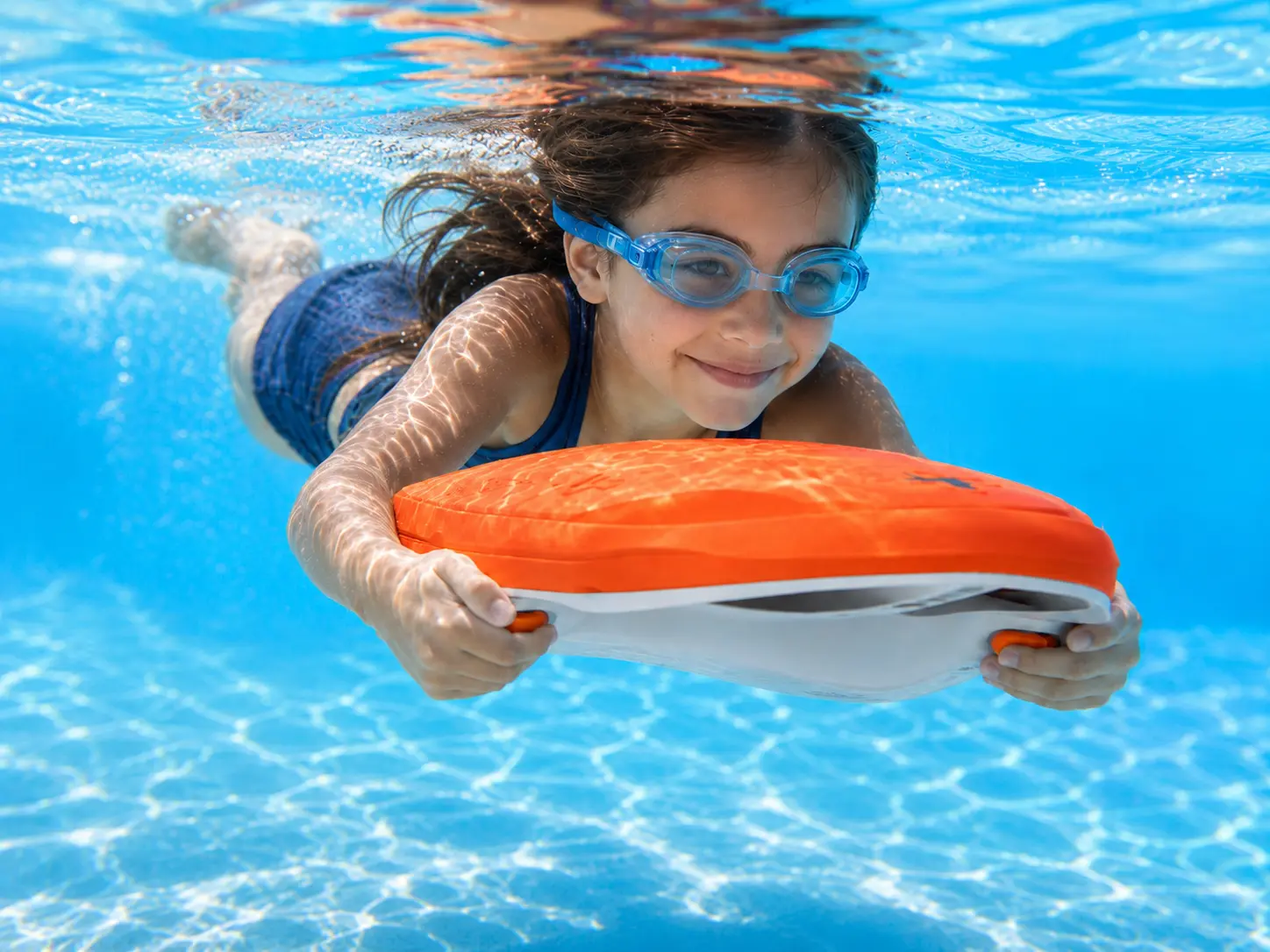 ALMARA - Child swimming with an orange water board just below the pool surface